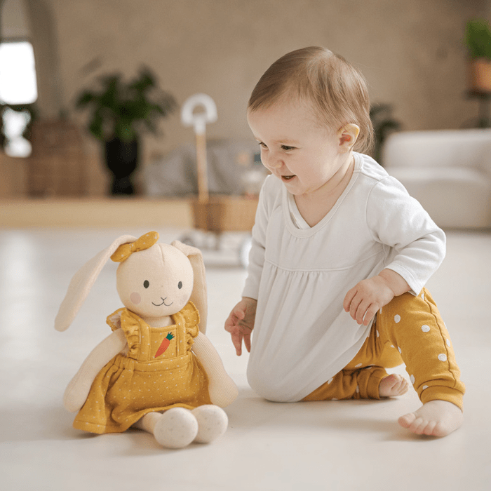 Kleinkind schaut Kuscheltier-Hasen aus Bio-Baumwolle mit gelbem Kleid an